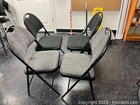 Four folding chairs, two grey and two black, arranged in a semi-circle showing seats and backs.