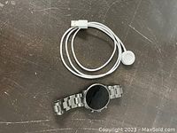 Fossil smartwatch lying flat next to white charging cable on dark surface.