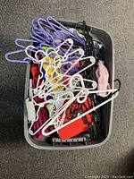Overhead view of a storage bin filled with assorted used plastic coat hangers in purple, white, black and other colors