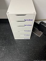 Front view of white Ikea Alex drawer unit showing 6 drawers with removable 'Sewing' vinyl labels