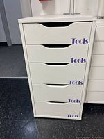 Front view of white IKEA Alex drawer unit with five drawers labeled 'Tools'.