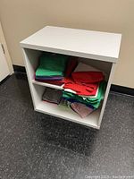 Front view of white Ikea Besta storage unit with a white shelf inside and colorful folded fabric stored on the shelves.