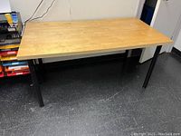 Full view of IKEA table with light wood grain top and black legs on black floor.