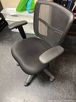 Black office swivel chair with mesh backrest and fabric seat shown from front angle on black floor.