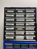 Two stacked plastic drawer units, the top with 18 small labeled drawers for various hardware parts, the bottom with larger blue/clear drawers.