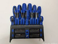 Complete screwdriver set with blue handles placed in black plastic wall-mountable holder.