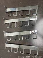 Four chrome metal slat wall hooks laid flat showing 5 hooks on each and attachment mounts on the back.