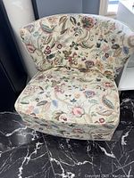 Front view of the small swivel chair showing cushioned floral fabric upholstery and wooden swivel base.