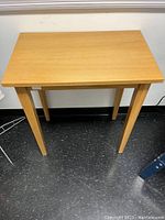 Front angled view of a tall rectangular teak veneer side table with four angled legs and visible minor wear on the surface.
