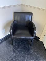 Front angle view of one chocolate brown faux leather tub chair with black legs on black tiled floor