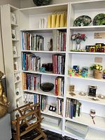 Two large white Ikea Billy bookcases filled with books, plates and decorative items