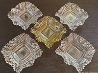 Six square glass candy dishes: five clear glass and one yellow glass, displaying diamond point pattern and scalloped edges, arranged on a dark surface.