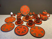 Full set laid out on table showing 25 pieces of red and green pottery tea service including plates, cups, teapot, salt and pepper, sugar and jam dishes.