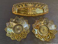 Top down photo showing two Federal Glass amber pedal bowls with intricate starburst and petal cut patterns, and one Hazel Atlas amber relish dish with elongated geometric cut design.