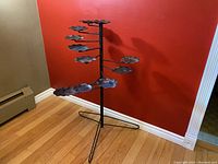 Full view of antique tiered swing arm plant stand showing 9 scalloped metal trays connected to arms radiating from a central vertical post with tripod base.