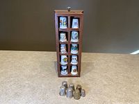 Full view of all 17 thimbles including 10 in wooden display case and 7 loose metal thimbles in front.