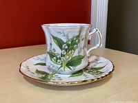 Lily of The Valley teacup and saucer set displayed on table showing floral design and gold trim.