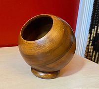 Front angle view of the wooden orb desk organizer showing its round shape, wood grain texture, and pencil holder opening.