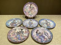 Six round Royal Doulton collector plates displayed on a flat surface with one plate on a stand in the back. Each plate depicts Asian-inspired artwork showing women in traditional clothing and scenery with floral and architectural motifs.