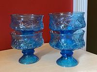 Four vintage Anchor Hocking azure blue footed dessert glasses stacked in two pairs, showing embossed rain and flower design on bowl sides and foot.