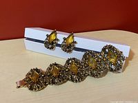 Vintage chunky metal bracelet with yellow diamond cut stones placed on a stand with matching clip on earrings.