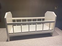Front angle view of the white wooden baby doll bed showing spindle rails and solid end panels.