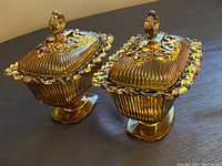 Two vintage Indiana Glass amber pedestal candy dishes with ornate open lace edge rims and matching lids with finial handles.