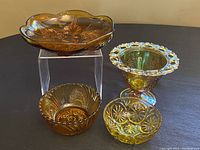 Four amber iridescent glass bowls displayed on black surface with two on clear stand.