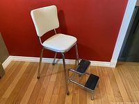 Front and right side view of the vintage kitchen chair step-stool showing the white vinyl seat and backrest, chrome legs, and two black step-stools attached to the sides.