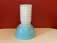 Stacked view with five white Fire King bowls stacked inside large turquoise Pyrex 402 bowl.