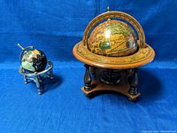 Front view showing both globes with wooden and metal stands on blue fabric background