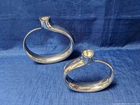 Two polished metal Nambe candlestick holders in modern circular design on blue backdrop, showing different heights and profile views.