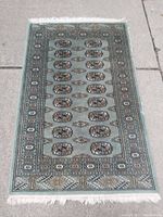 Full view of the green vintage Bokhara rug laid flat on concrete, showing overall pattern and condition.