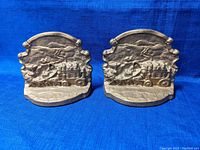 Front view of both bronze bookends showing detailed stage coach designs with horses and drivers on a mountainous background.