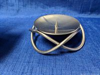 Photo of the Georg Jensen candle holder showing its polished stainless steel with circular top and spike for candle placement, sitting on a blue fabric background.