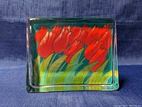 Front view of a rectangular glass paperweight showing a red tulip floral design on a green background.