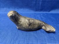 Side view of the carved stone seal on a blue fabric, showing shape and tail details.