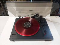 Black Kenwood KD-291R turntable with transparent dust cover open, playing a red translucent vinyl record.