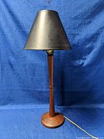 Full front view of the lamp showing full lamp height and tapered teak wood base with black shaded top.