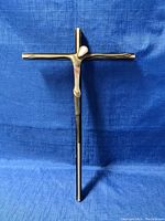 Full view of the mid century modernist iron crucifix against a blue background, showing the entire cross and attached abstract figure.