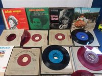 Photo showing 4 vinyl records with covers displayed on top, mainly featuring red color labels and sleeves by Divinda Rodrigues, Leon Mendes, Sylvie Vartan, Fatima Molina, with records partially out of cardboard sleeves.