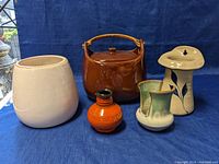Wide front view of all five ceramic pieces arranged on blue cloth background, showing sizes, shapes and colors
