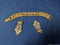 Photo of gold-tone rhinestone bracelet alongside matching earrings on blue fabric background.