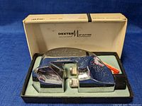 Top angle view of chrome Dexter Mat Cutter on original box showing surface spots and wear.