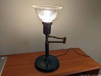 Front view of the vintage swing arm lamp lit, showing the base and pleated glass shade.