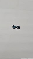 Pair of natural heart-shaped blue sapphires with teal undertones placed on a neutral background.