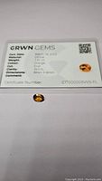 Photo showing the oval cut citrine gemstone with certification card detailing the gem's specifications including cut, clarity, weight, color, dimensions, and certification date.