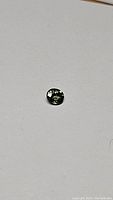 Top view of the small oval green sapphire gemstone visible against a plain light background showing its facets and color.