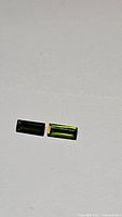 Two matched baguette cut bright green tourmaline gemstones on a white background.