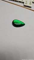 Front view of pear-shaped green labradorite gemstone showing vibrant fluorescent green color and smooth cabochon finish.